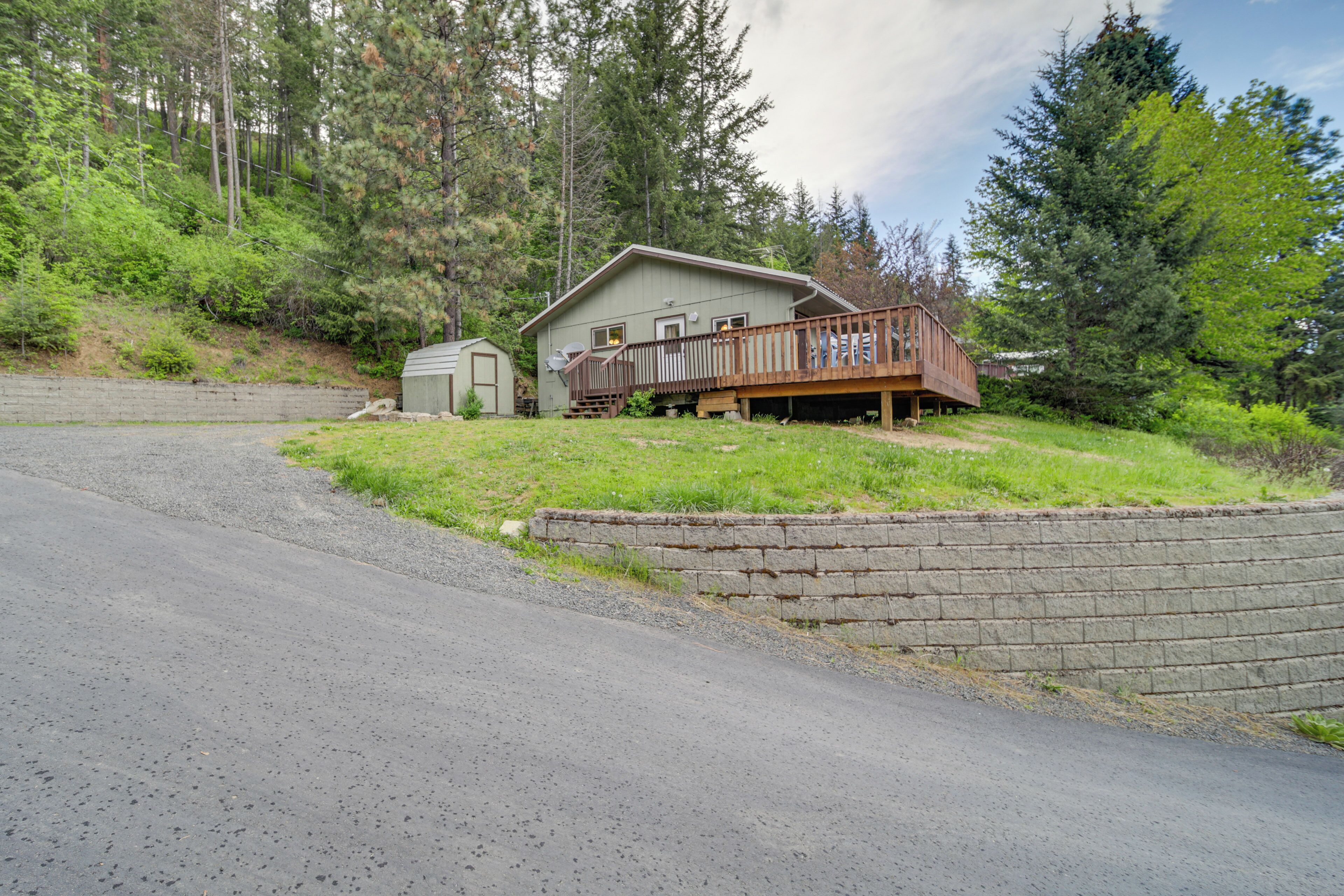 A two-story house with a deck, a garage, and a small shed, surrounded by a forested area.