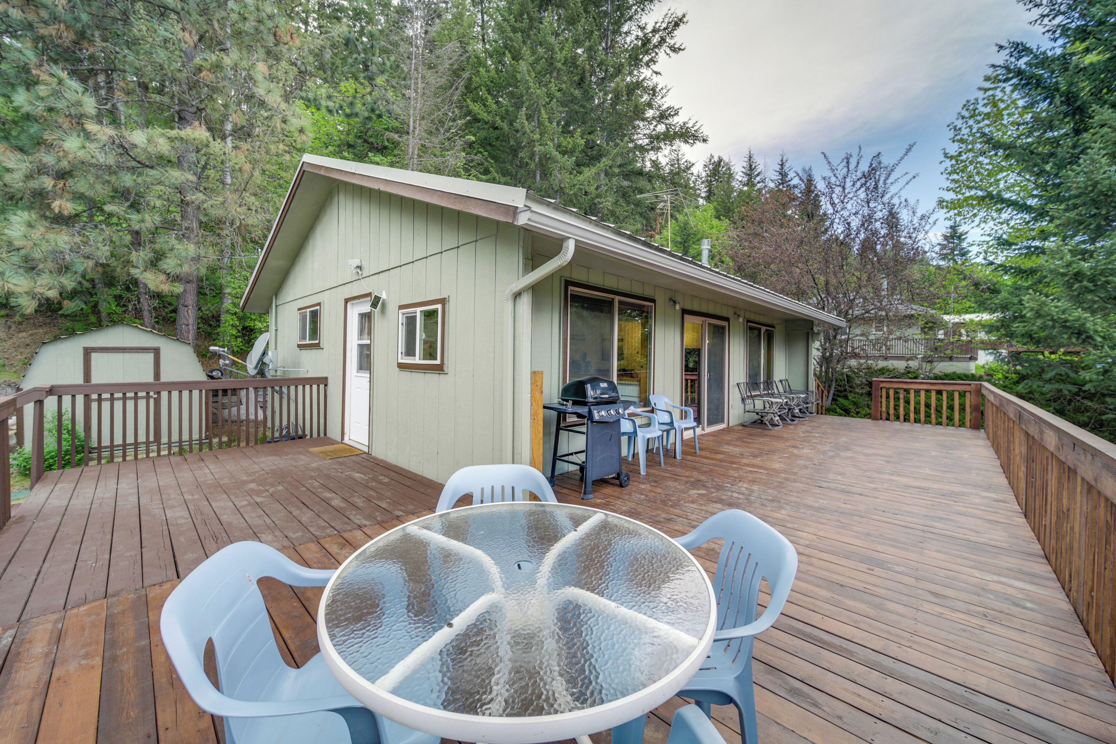 A wooden deck with a glass table and chairs, a barbecue grill, and a small building with a door and windows.