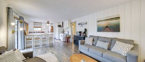 A spacious living area with a grey sofa, a wooden coffee table, and a kitchen in the background.