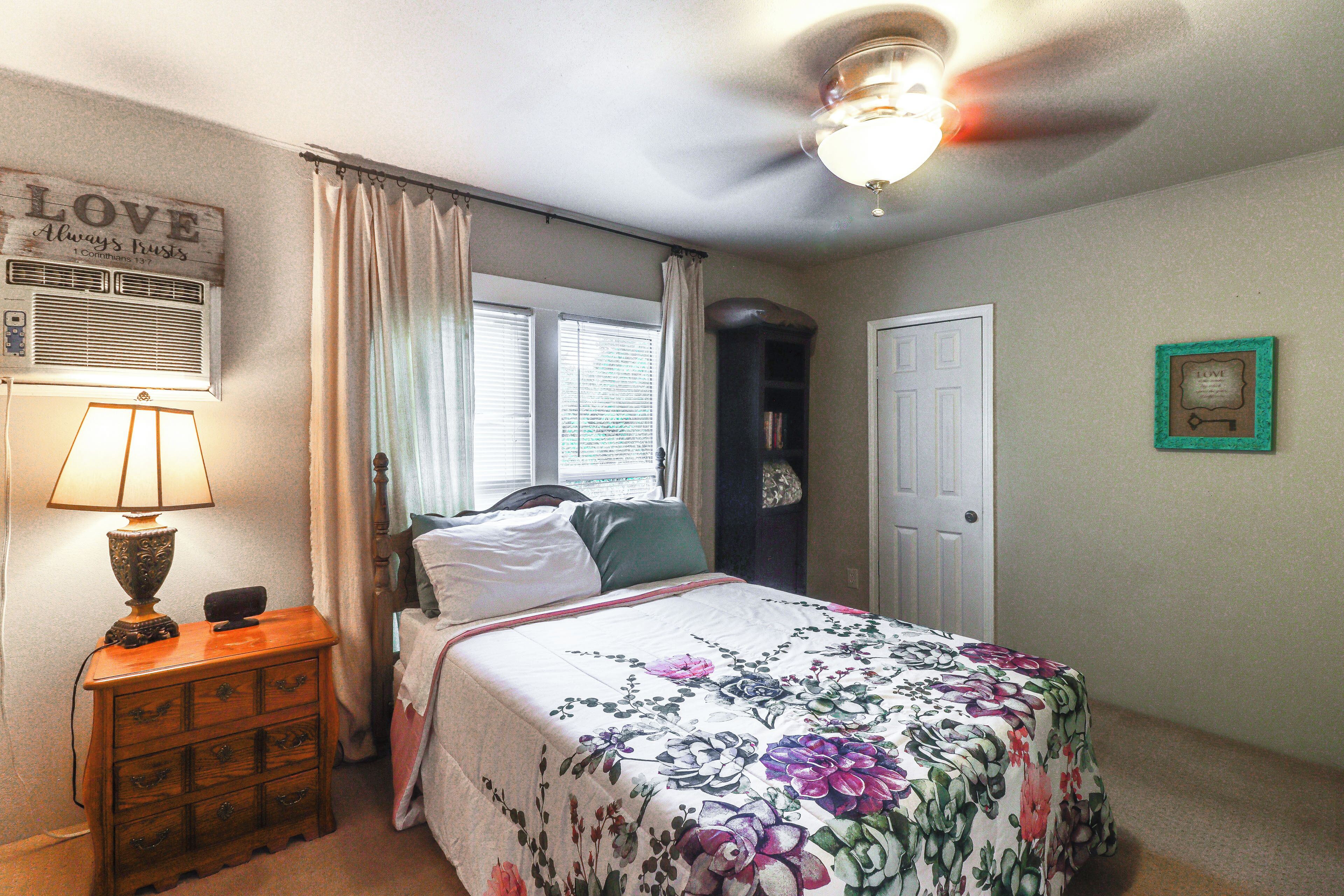 A bedroom with a bed, a nightstand, a lamp, a ceiling fan, and a window with curtains.