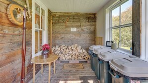 Un intérieur rustique en bois, avec une table en bois, un vase rempli de fleurs, une pile de bois de chauffage et des poubelles.