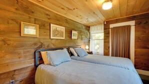 Une chambre rustique en bois avec deux lits, des tableaux encadrés accrochés au mur et une fenêtre avec des rideaux.