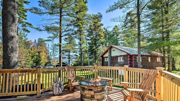 A wooden deck with a stone fire pit, wooden chairs, and a cabin in the background. - Lake Pleasant Access! Speculator Cottage w/ Deck (Speculator)