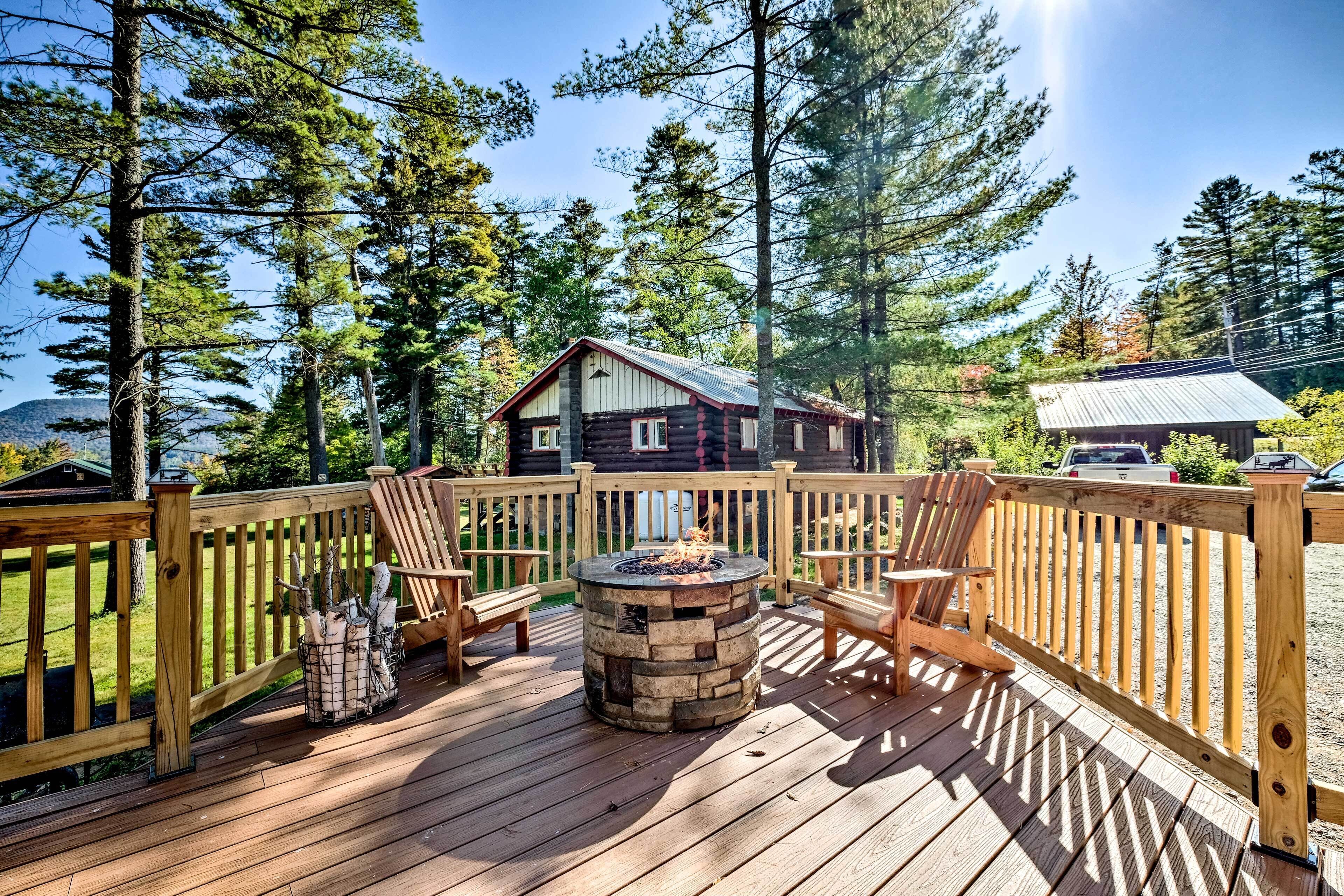 A deck with a stone fire pit, wooden chairs, and a view of a cabin.