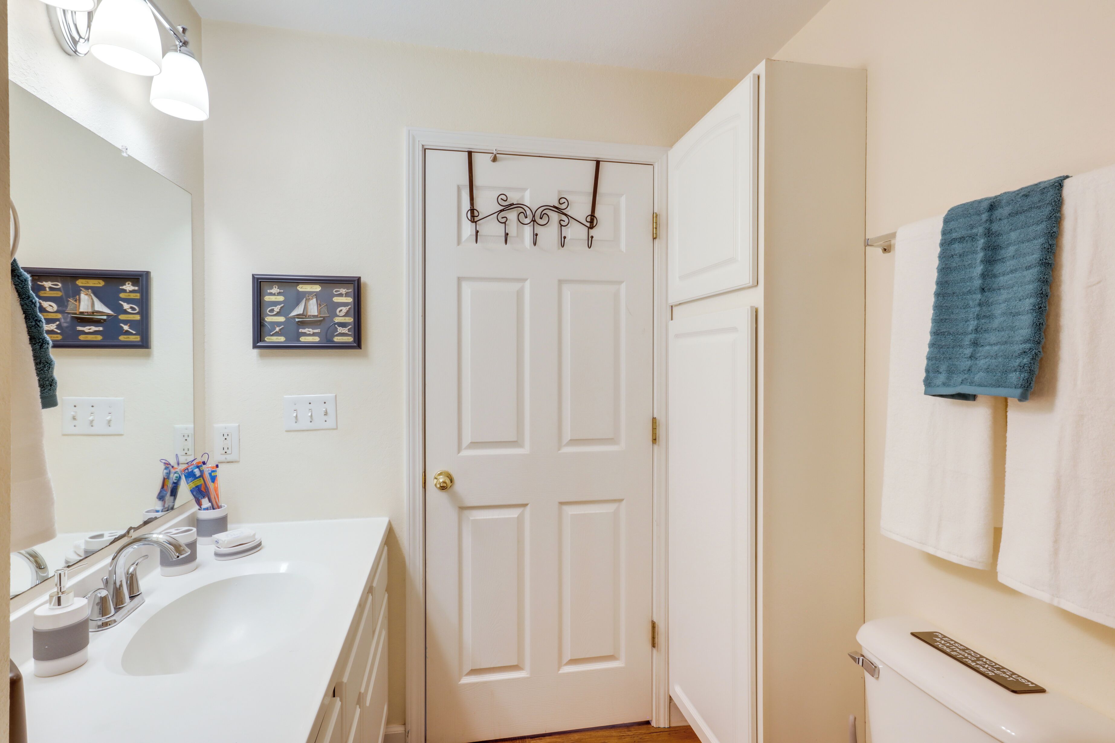 A bathroom with a white sink, a mirror, a towel rack with a blue towel, and a toilet with a sign on the tank.