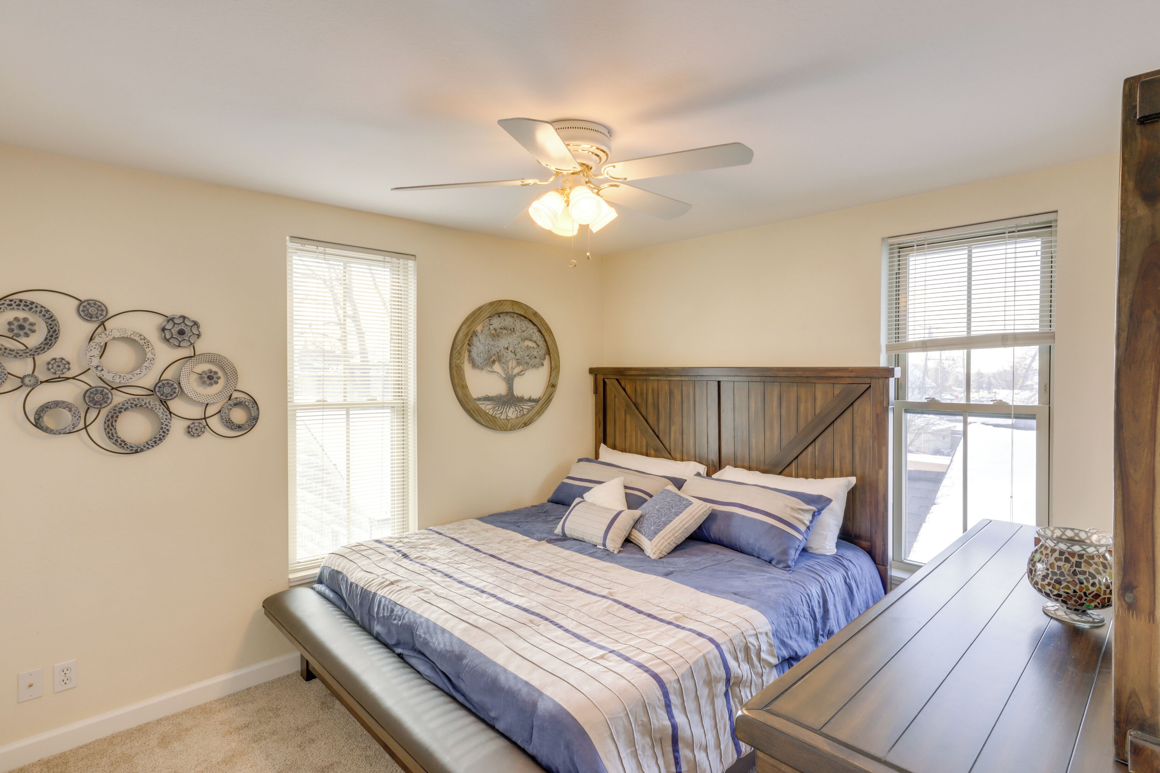 A bedroom with a bed, a ceiling fan, a window, and a wall decoration.