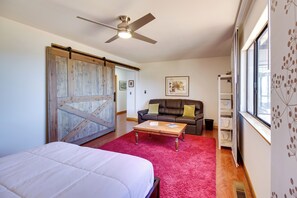 A bedroom with a bed, a red rug, a ceiling fan, a brown leather couch, and a window with blinds.