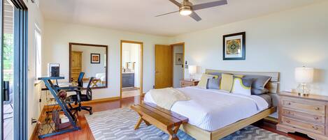 A bedroom with a bed, desk, and chair, a ceiling fan, and a view through an open door.