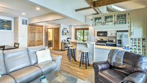 A spacious living area with a leather sofa, a dark leather armchair, and a kitchen with white cabinets and a bar area. - Lakefront Plymouth Cottage w/ Private Hot Tub (Plymouth)