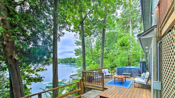 A wooden deck with outdoor furniture, overlooking a lake with boats. - Lakefront Plymouth Cottage w/ Private Hot Tub (Plymouth)