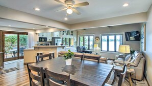 A spacious kitchen with modern appliances, a dining area with a wooden table and chairs, and a cozy seating area with a sofa and a TV mounted on the wall. - Lakefront Plymouth Cottage w/ Private Hot Tub (Plymouth)