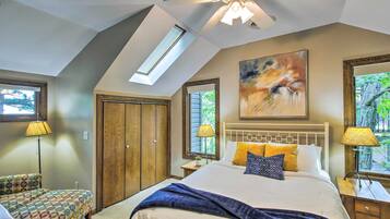 Une chambre avec un puits de lumière, un lit avec de nombreux oreillers, une table de chevet, une armoire en bois et une fenêtre donnant sur des arbres.
