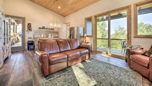 A spacious living room with a leather sofa, a patterned rug, and a large window providing a view of the outdoors. - Contemporary Home w/ Deck & Mountain Views! (Waynesville)