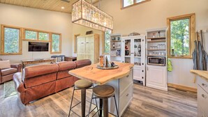 A spacious living area with a large brown leather couch, a wooden dining table with stools, a kitchen with white cabinets and a microwave, and a ceiling fan. - Contemporary Home w/ Deck & Mountain Views! (Waynesville)