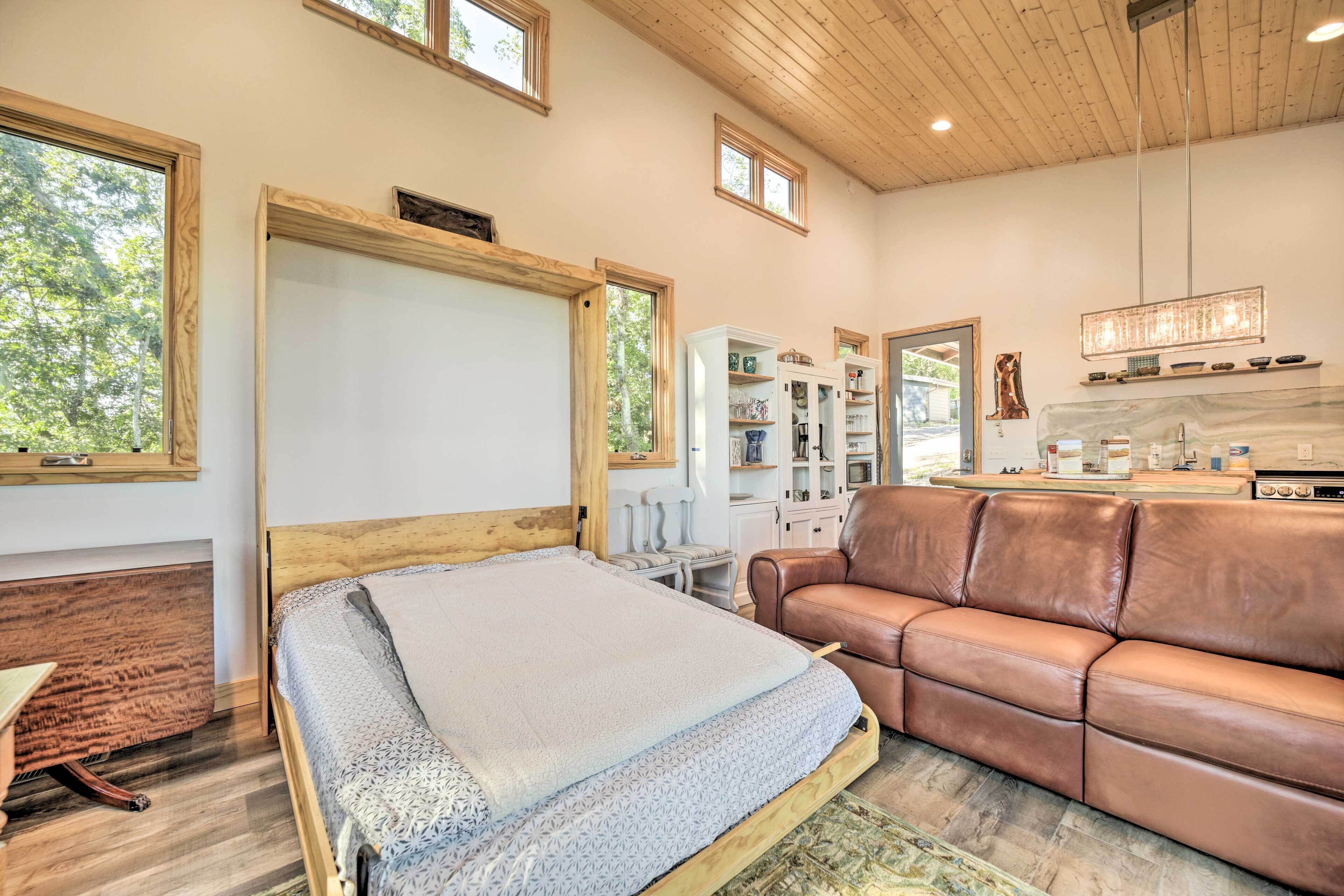 A bedroom with a bed, a leather sofa, a wooden headboard, a white cabinet, and a window.