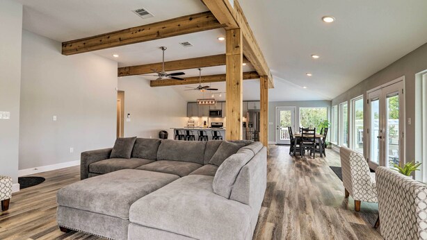 A spacious living area with a sectional sofa, wooden beams, a ceiling fan, and a view into the kitchen.