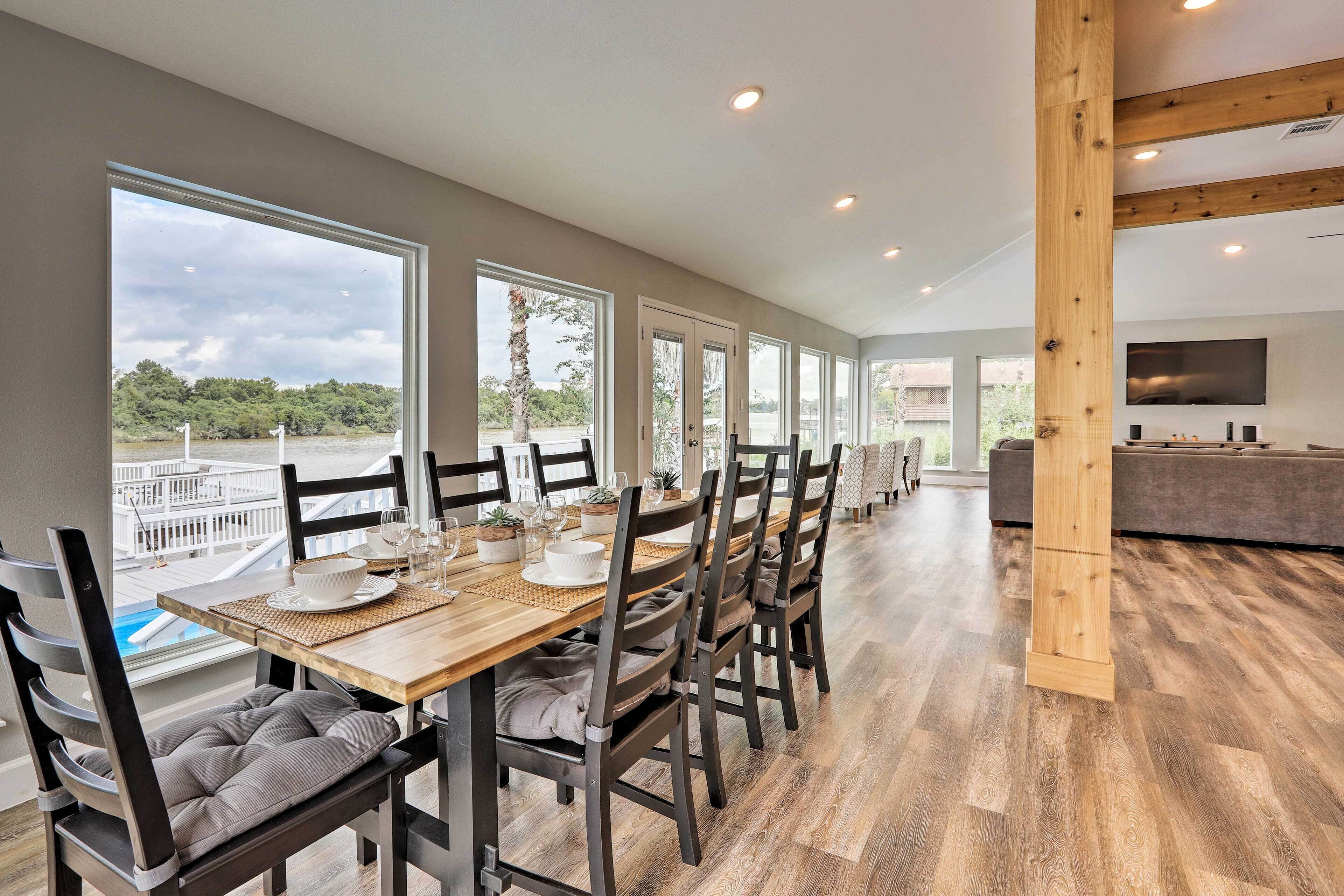 A spacious dining area with a long table, multiple chairs, and a view of a pool and trees.