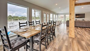 A spacious dining area with a long table, multiple chairs, and a view of a pool and trees.