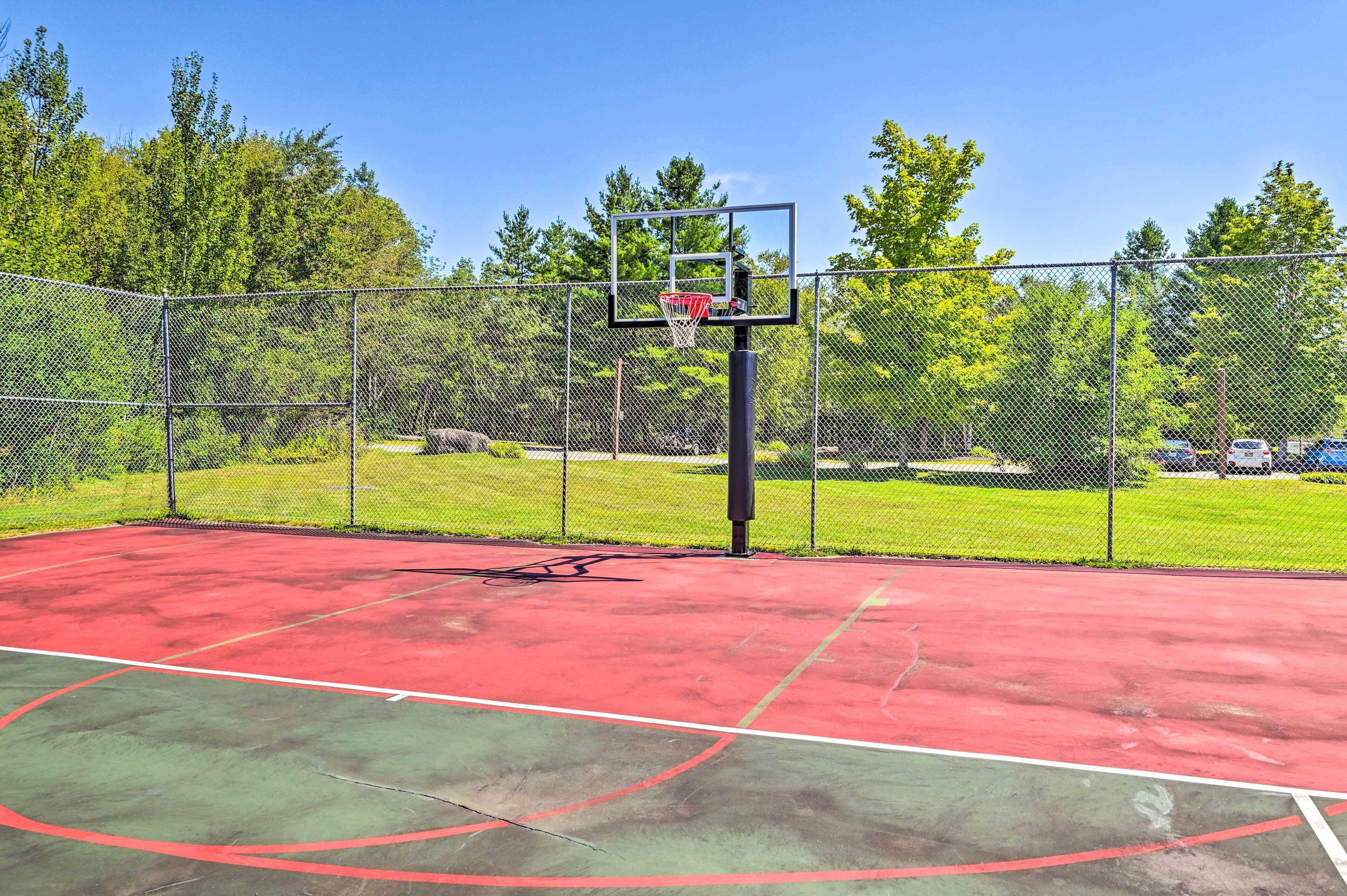 An outdoor basketball court with a chain-link fence, a basketball hoop, and a red and green playing surface.
