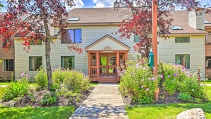 A house with a front porch, a wooden pathway leading to the entrance, and a garden with various plants and flowers. - Comfortable Dover Apartment: Walk to Mt Snow! (West Dover)