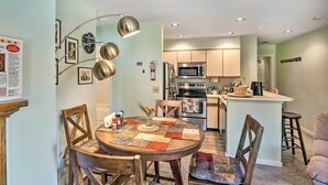 A modern kitchen with stainless steel appliances, a dining area with a round table and wooden chairs, and a small island with bar stools. - Comfortable Dover Apartment: Walk to Mt Snow! (West Dover)