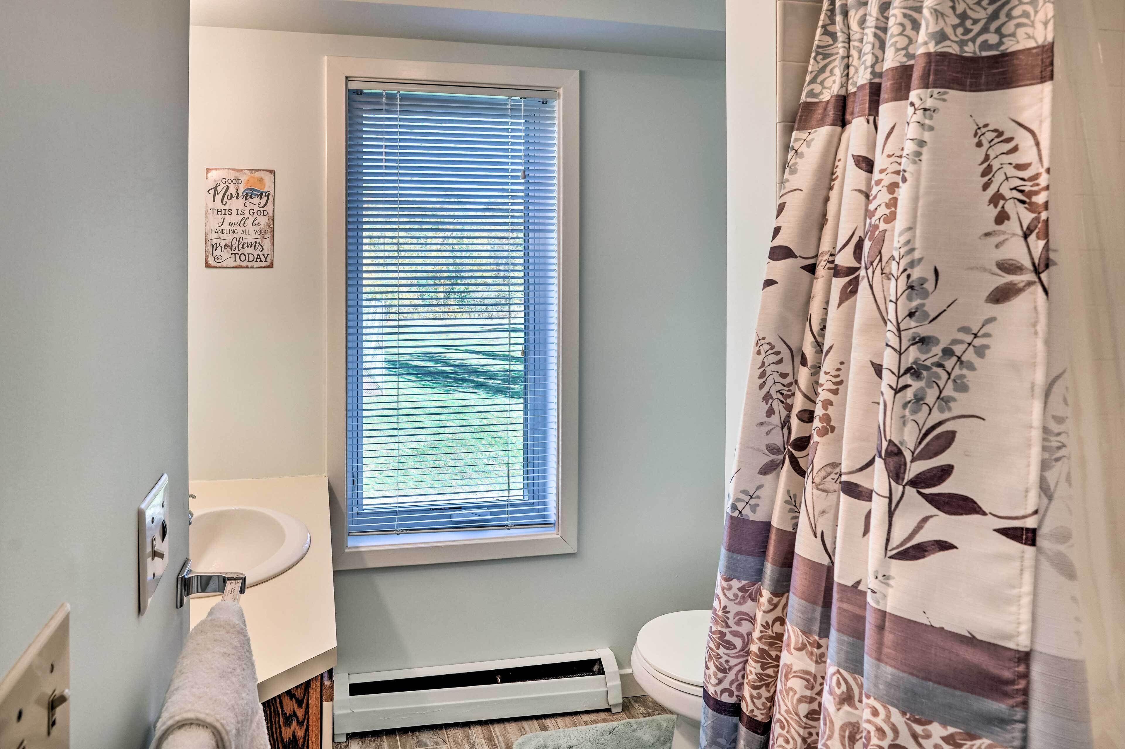 A bathroom with a window, a sink, a toilet, and a shower curtain.
