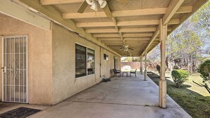 A covered patio area with a concrete floor, a ceiling fan, and a view of a backyard with a wooden fence and trees. - Inviting Bakersfield Home w/ Spacious Yard! (Bakersfield)