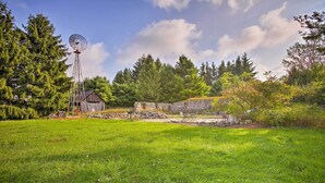 A grassy field with a windmill, a stone wall, and a wooden building. - Leelanau Country Cottage ~ 4 Mi to Suttons Bay! (Suttons Bay)