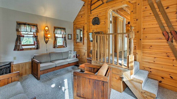 A cozy cabin interior with a wooden staircase, a sofa, and skis mounted on the wall. - Leelanau Country Cottage ~ 4 Mi to Suttons Bay! (Suttons Bay)