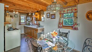 A rustic kitchen with wooden beams, a gas stove, and a dining area with a glass table and chairs. - Leelanau Country Cottage ~ 4 Mi to Suttons Bay! (Suttons Bay)