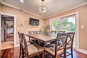 A dining area with a large wooden table and chairs, a chandelier, a TV mounted on the wall, and a window with a view of the outdoors. - Fenced Yard: Fox River Grove Home, Dogs Welcome (Fox River Grove)
