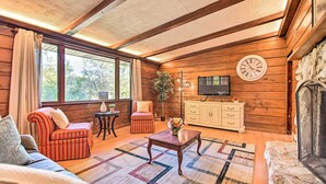 Een gezellige woonkamer met houten wanden, een open haard, een televisie en een groot raam met gordijnen.