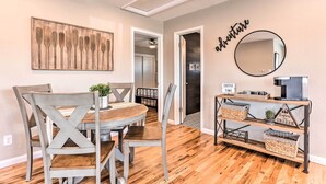 A dining area with a wooden table and chairs, a wall-mounted mirror, and a shelf with baskets.