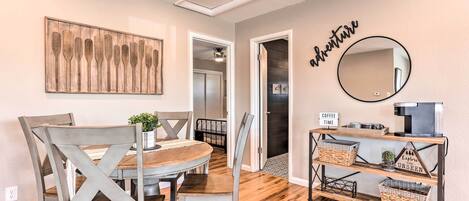 A dining area with a wooden table and chairs, a wall-mounted mirror, and a shelf with baskets.