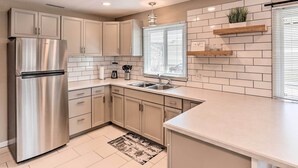 A modern kitchen with stainless steel appliances, white cabinets, and a tiled backsplash.