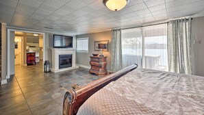A bedroom with a large bed, a television, a fireplace, and a view of the outdoors.
