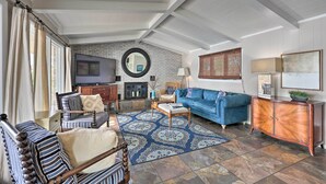 A spacious living room with a fireplace, a blue sofa, a striped armchair, and a wooden cabinet.