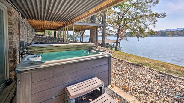A hot tub under a wooden pergola with a view of a lake and trees.