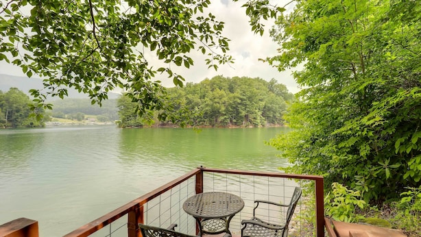 A deck with a table and chairs overlooking a lake, surrounded by dense greenery. - Lakefront Butler Retreat w/ Hot Tub & Dock! (Butler)
