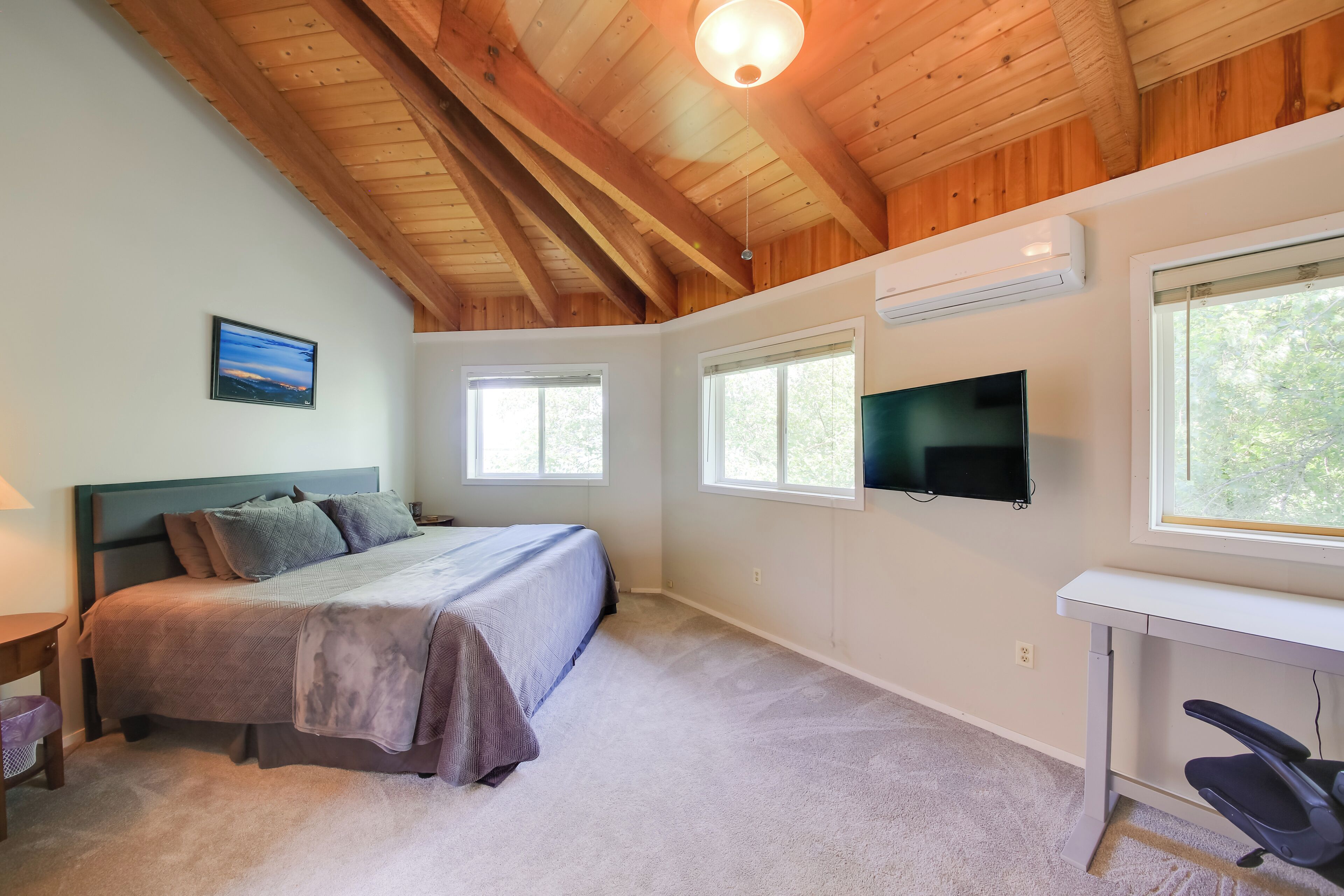 A bedroom with a bed, a desk, a TV, and windows.