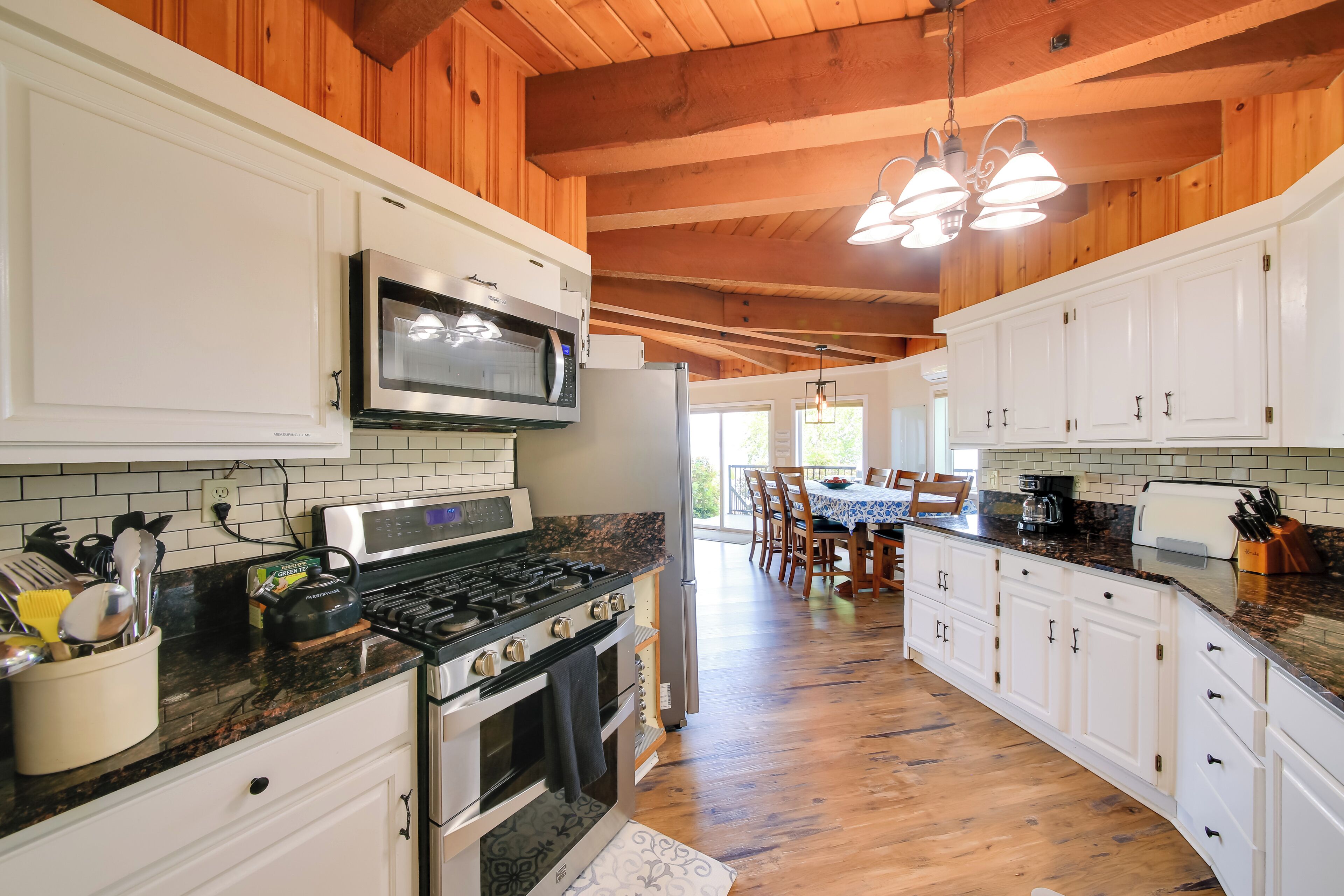 A kitchen with white cabinets, a microwave, stove, and a refrigerator. There is a dining area with a table and chairs.