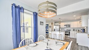 A dining area with a table set for four, a kitchen in the background, and a blue curtain on the window. - Freshly Remodeled Beach House, Steps to Shore (Sunset Beach)