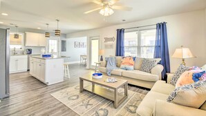 A modern living room with a sofa, coffee table, and a kitchen area with white cabinets and a central island. - Freshly Remodeled Beach House, Steps to Shore (Sunset Beach)