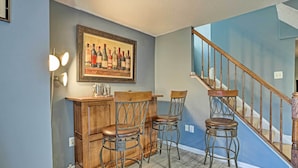 A kitchen with wooden bar stools, a bar counter, and a framed wine bottle painting on the wall.