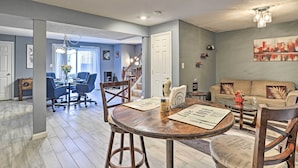 A spacious living area with a dining table, chairs, and a sofa. There is a staircase leading to another level, and a door to the left.
