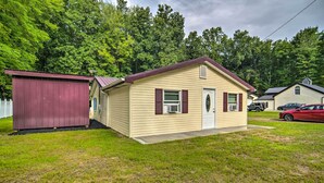 A single-story mobile home with a red roof and beige siding, a small porch, and a garage. - Jamestown Retreat w/ Hot Tub - Walk to Lake! (Westford)