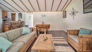 A living room with a wooden coffee table, a sofa, and a wooden dining table. - Jamestown Retreat w/ Hot Tub - Walk to Lake! (Westford)