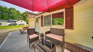 A covered patio with wicker furniture, a table, and a red umbrella. - Jamestown Retreat w/ Hot Tub - Walk to Lake! (Westford)