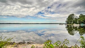 A calm lake with a dock and boats, surrounded by trees and vegetation. - Jamestown Retreat w/ Hot Tub - Walk to Lake! (Westford)