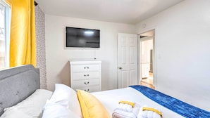 Een hotelkamer met een bed, een dressoir, een televisie en een deur die naar een andere kamer leidt.